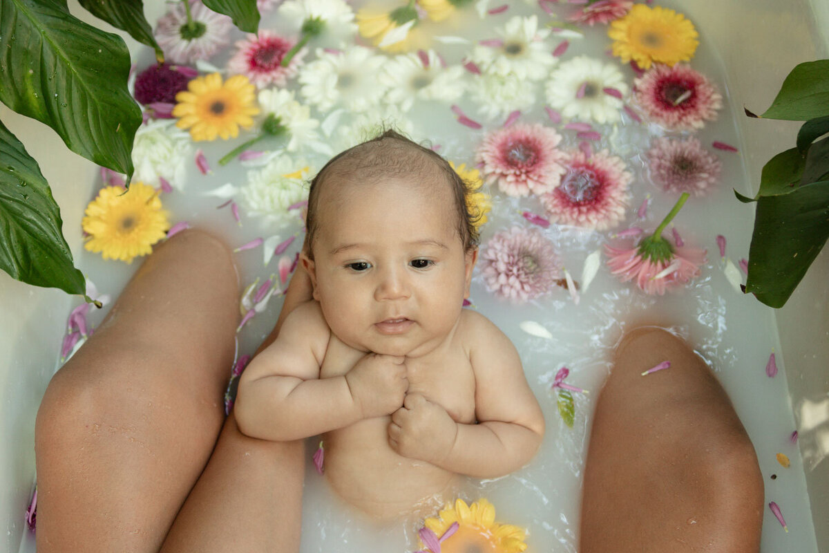 Close-up of a baby laying in a milk bath surrounded by flowers