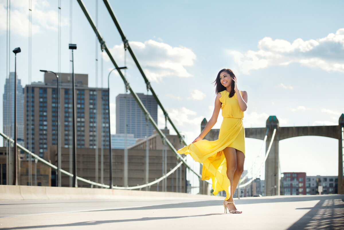 senior photo of girl in yellow dress standing on bridge in Minnapolis