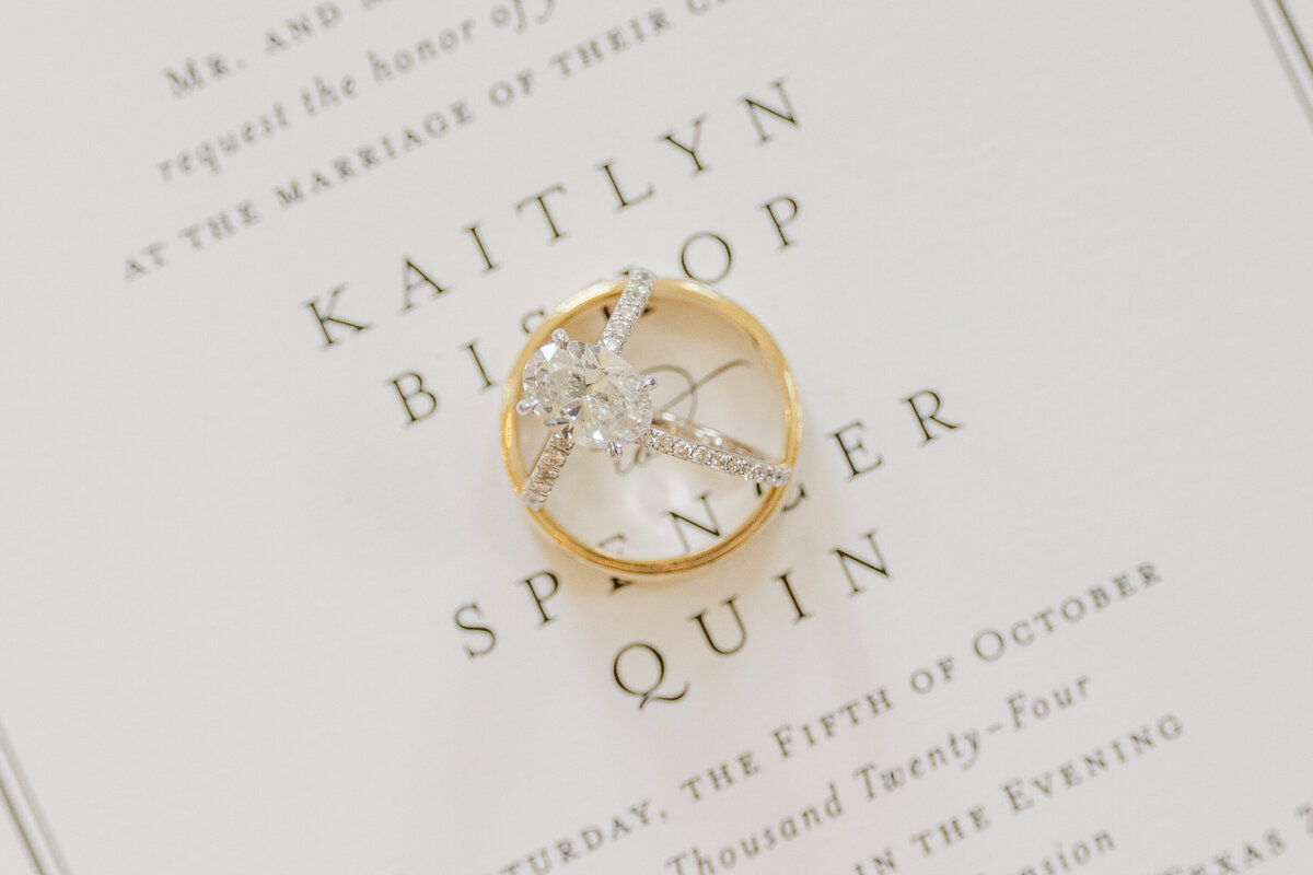 A delicate diamond engagement ring and gold wedding band are artfully styled atop a refined invitation suite. This luxury wedding flatlay, captured in a light and airy style, is perfect for brides planning a classic wedding near Coppell, Frisco, or Flower Mound, TX. Ideal for showcasing timeless details with an editorial flair.