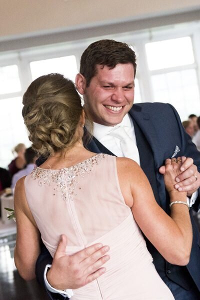 A groom smiles broadly as he shares a dance with his mother, captured by Colorado wedding photographer, Two One Photography.
