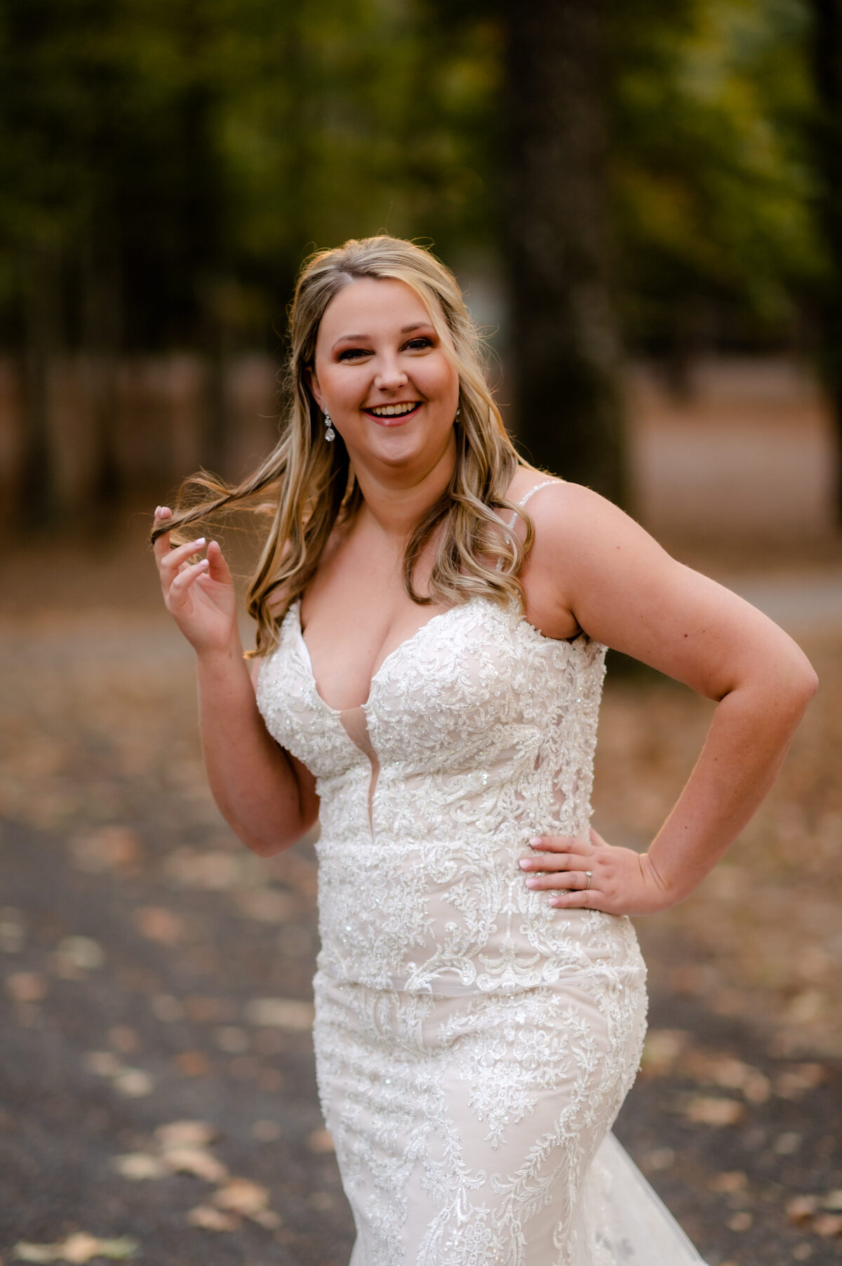 blonde bride standing with one hand on her hip and the other playing with her hair as she laughs during her forest bridal session