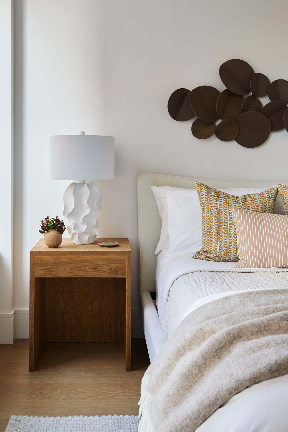 Neutral creams and white bedding with wooden side table and white lamp
