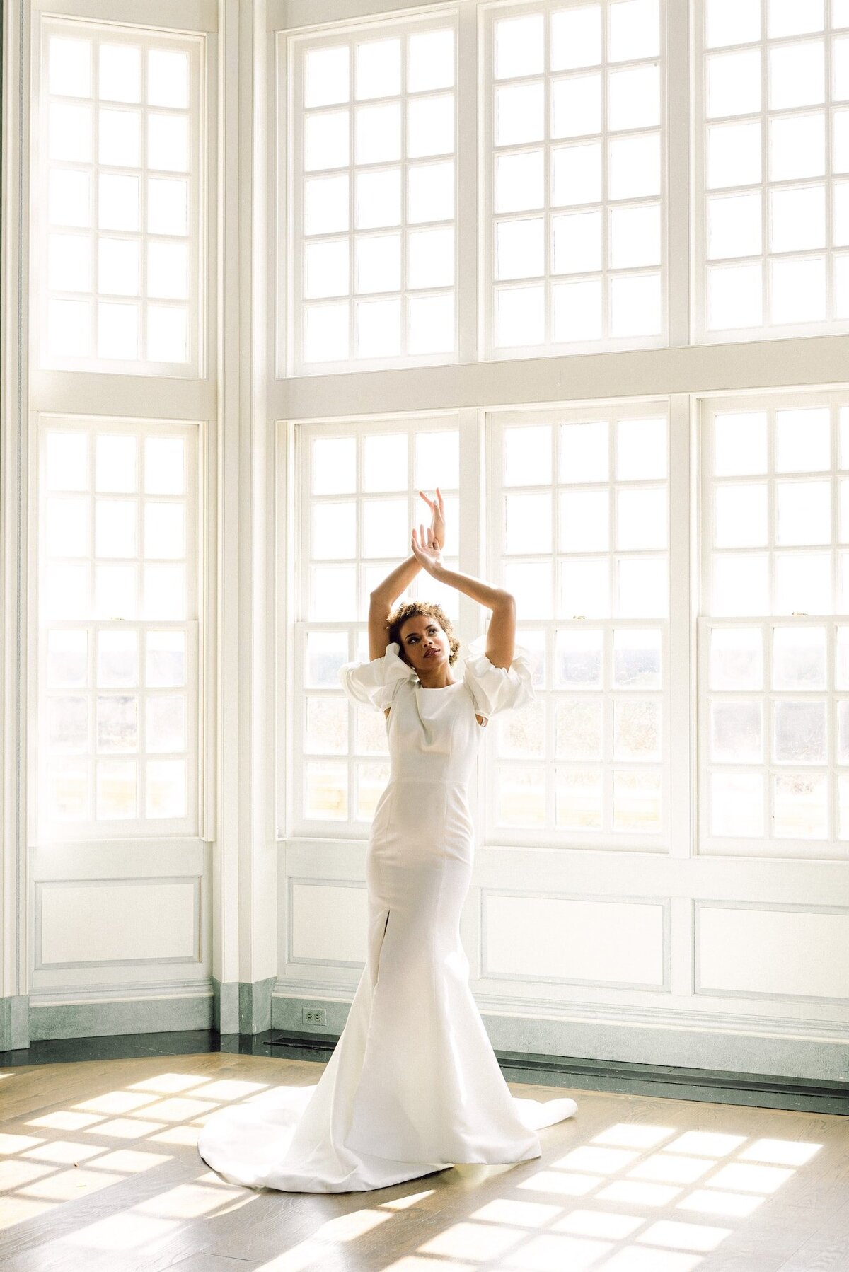 Bride posing with arms up in front of large wall of windows