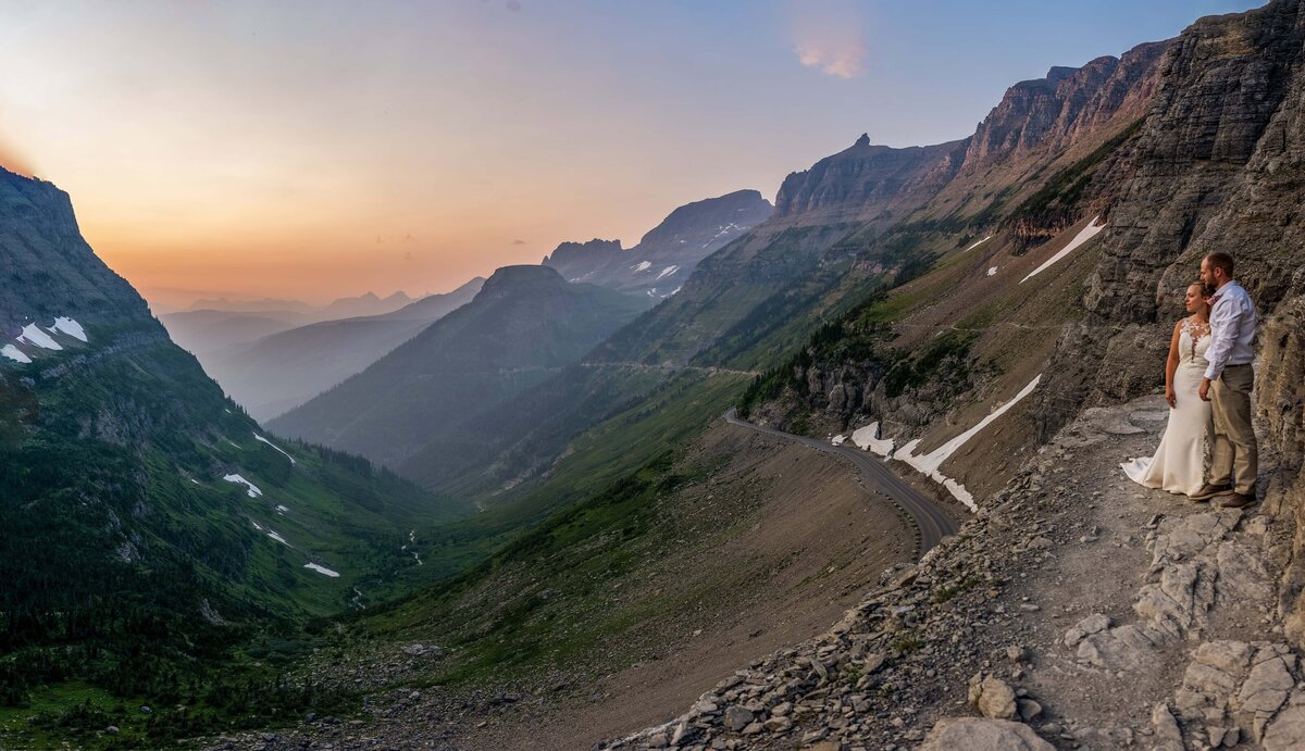 Eloping couple stands on Highline Trail overlooking Going to The Sun Road. 