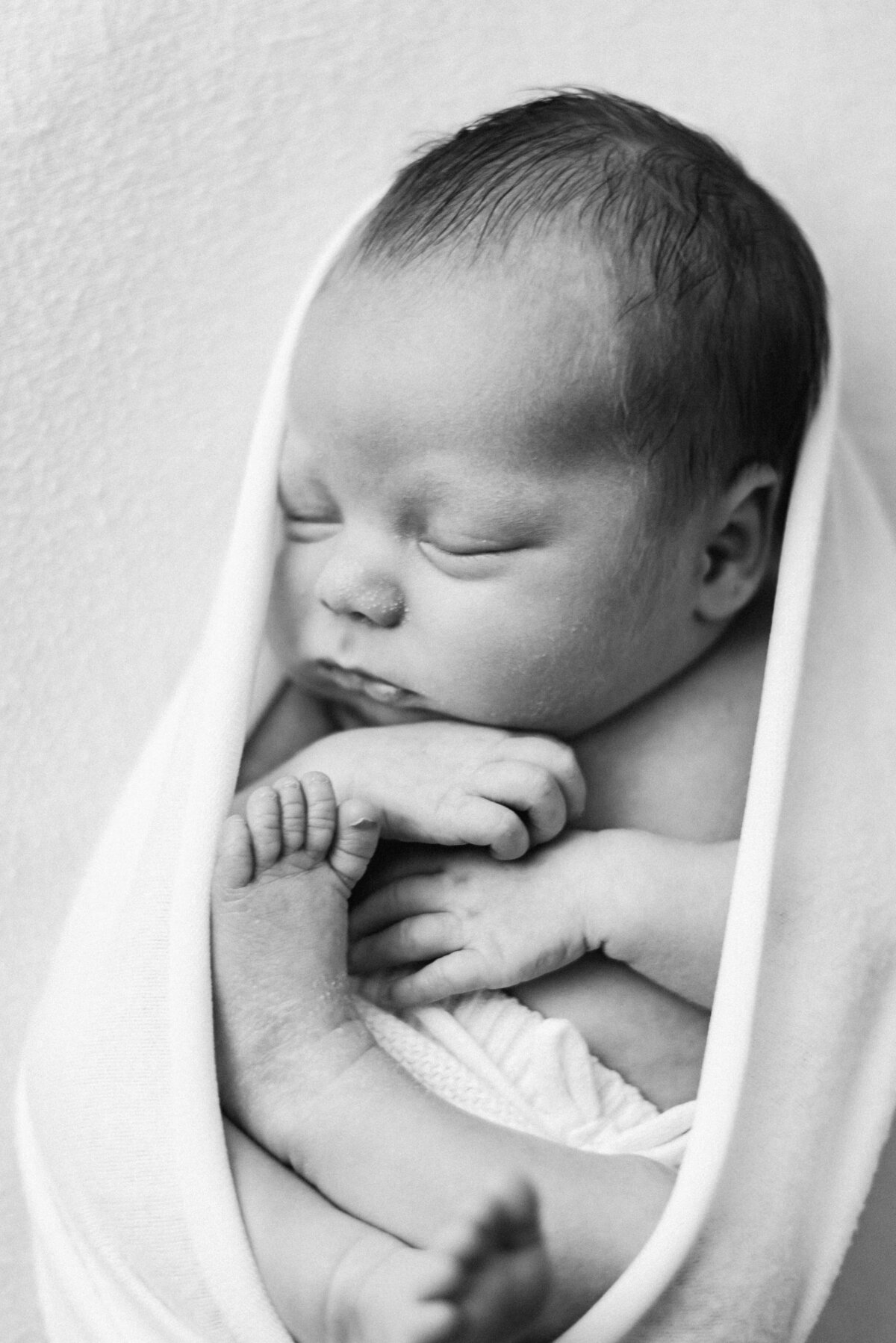 a newborn baby boy cuddled up in a blanket at Billingshurst newborn photoshoot
