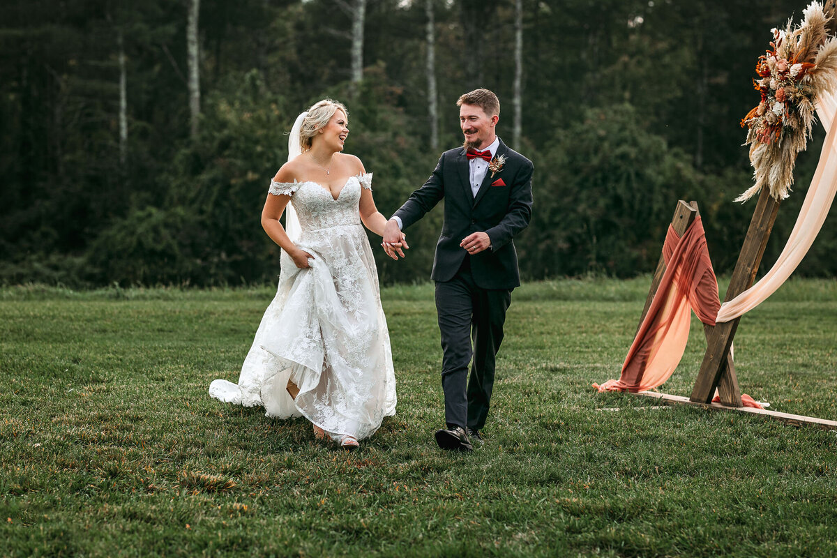 Joyful bride and groom walking together in a field in Sanborn Hill Farm by Lisa Smith Photography
