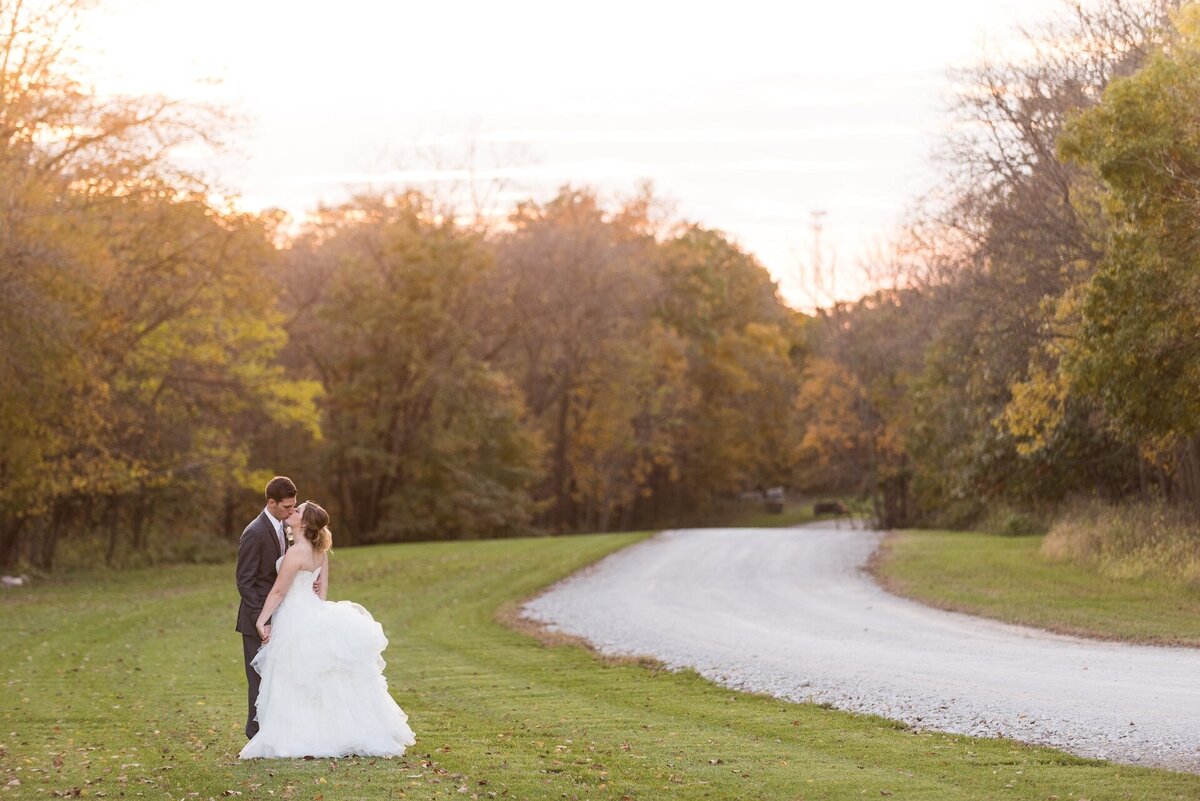 newlyweds kissing in wedding attire with a sunset and trees in the background