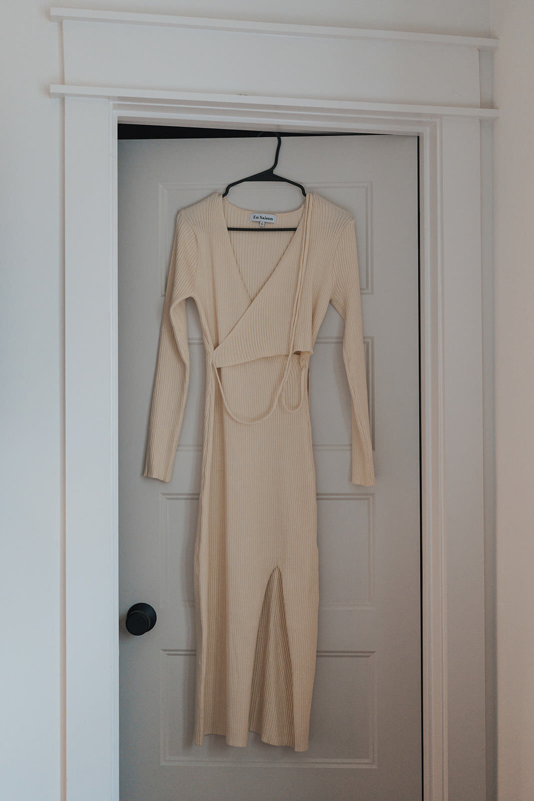 White wedding dress hangs in a hanger from the door