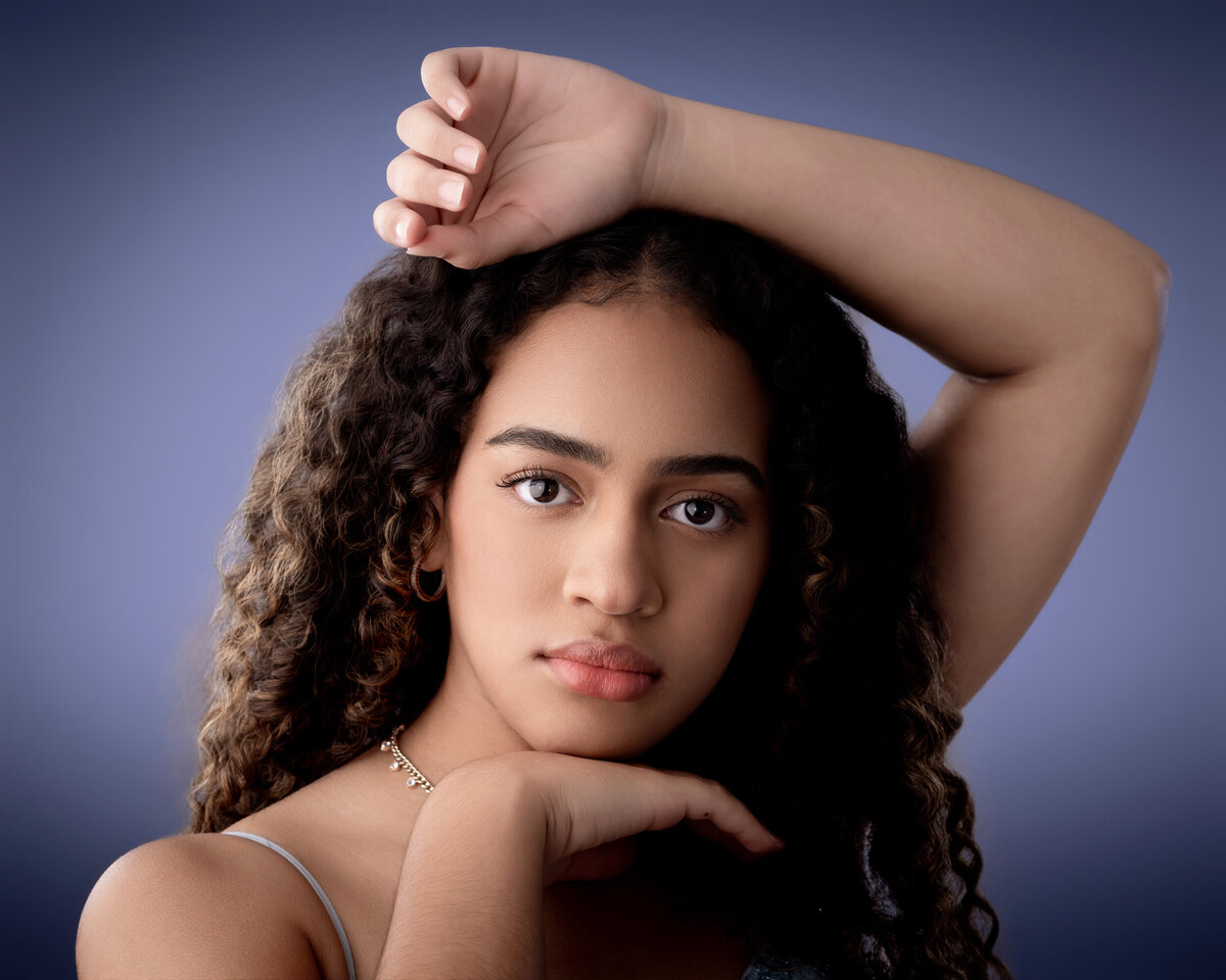 Teenage girl with curly hair posing with arm raised, against a blue background.