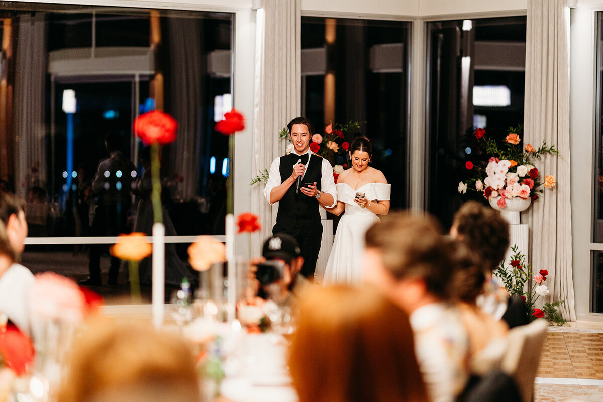 Bride and Groom across a room while they give a speech to their loved ones at their wedding
