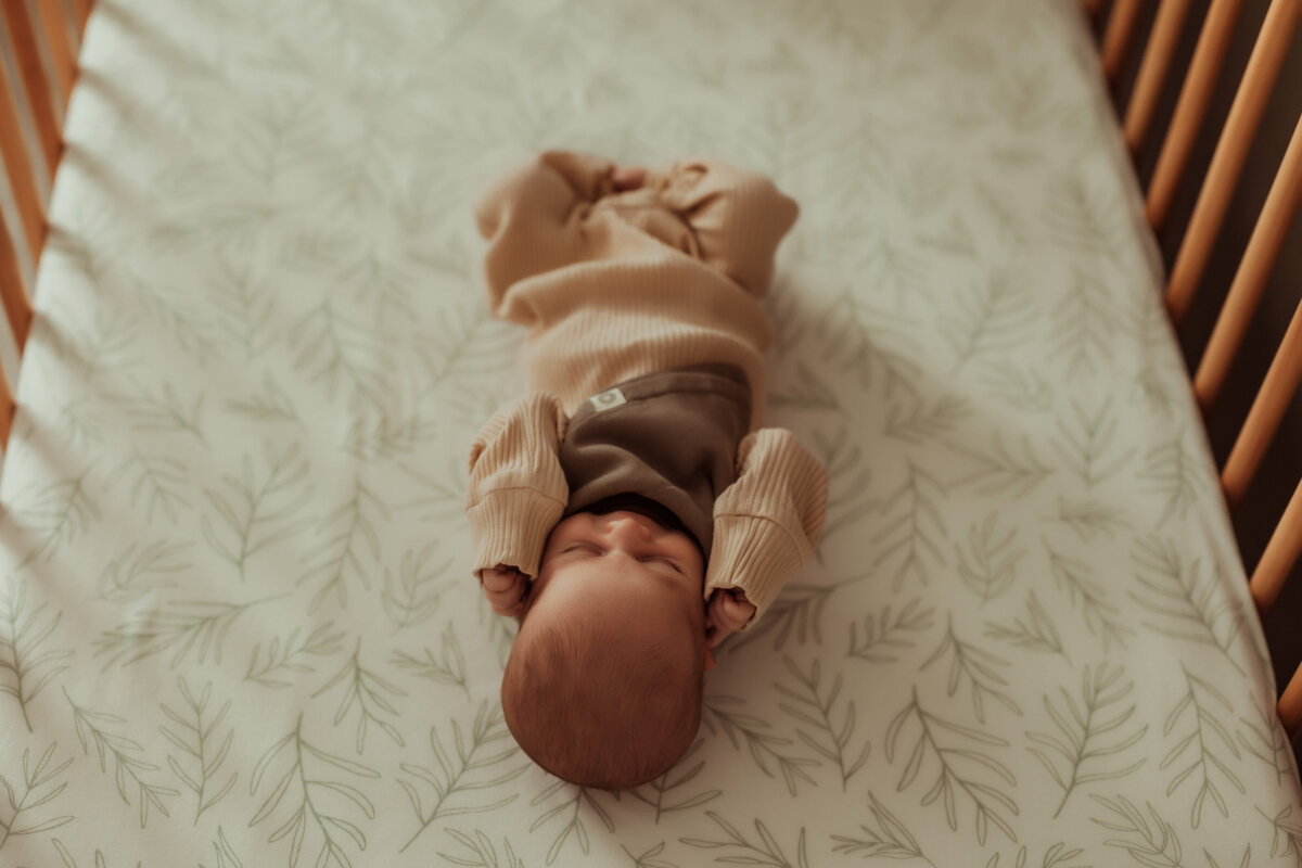 newborn baby boy lays on back in his crib