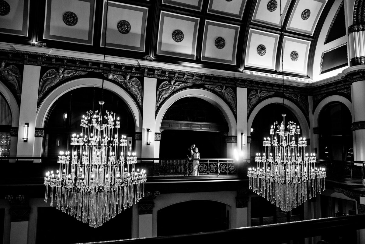 Dramatic black and white photo of couple on the balcony with the chandeliers framing them