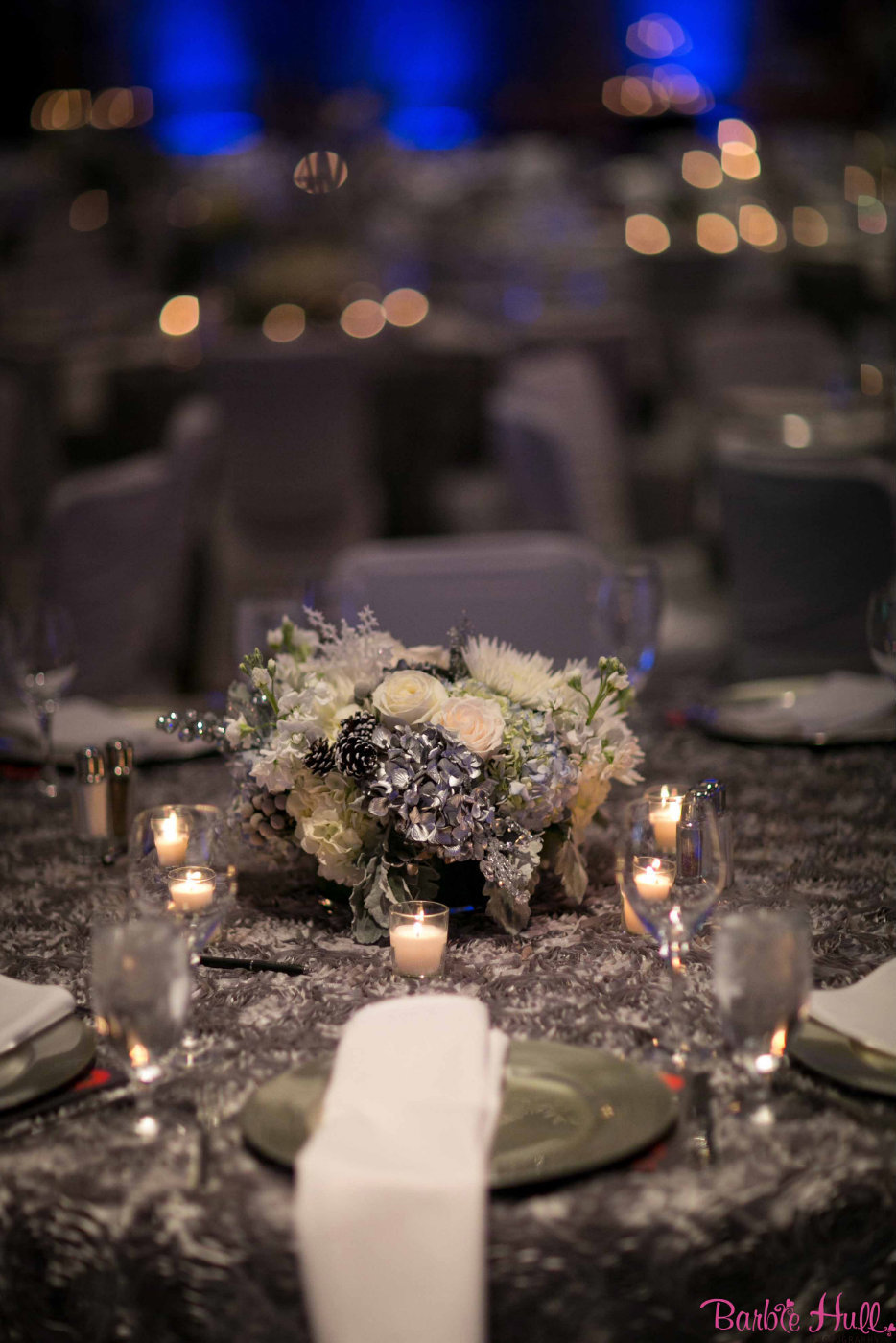 low centerpiece of silver painted hydrangea, white roses, silver stars on silver linen with votive candles, silver charger plate