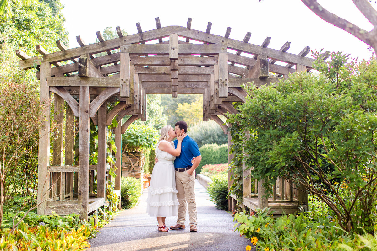 couple kissing in front of trellis at arboretum