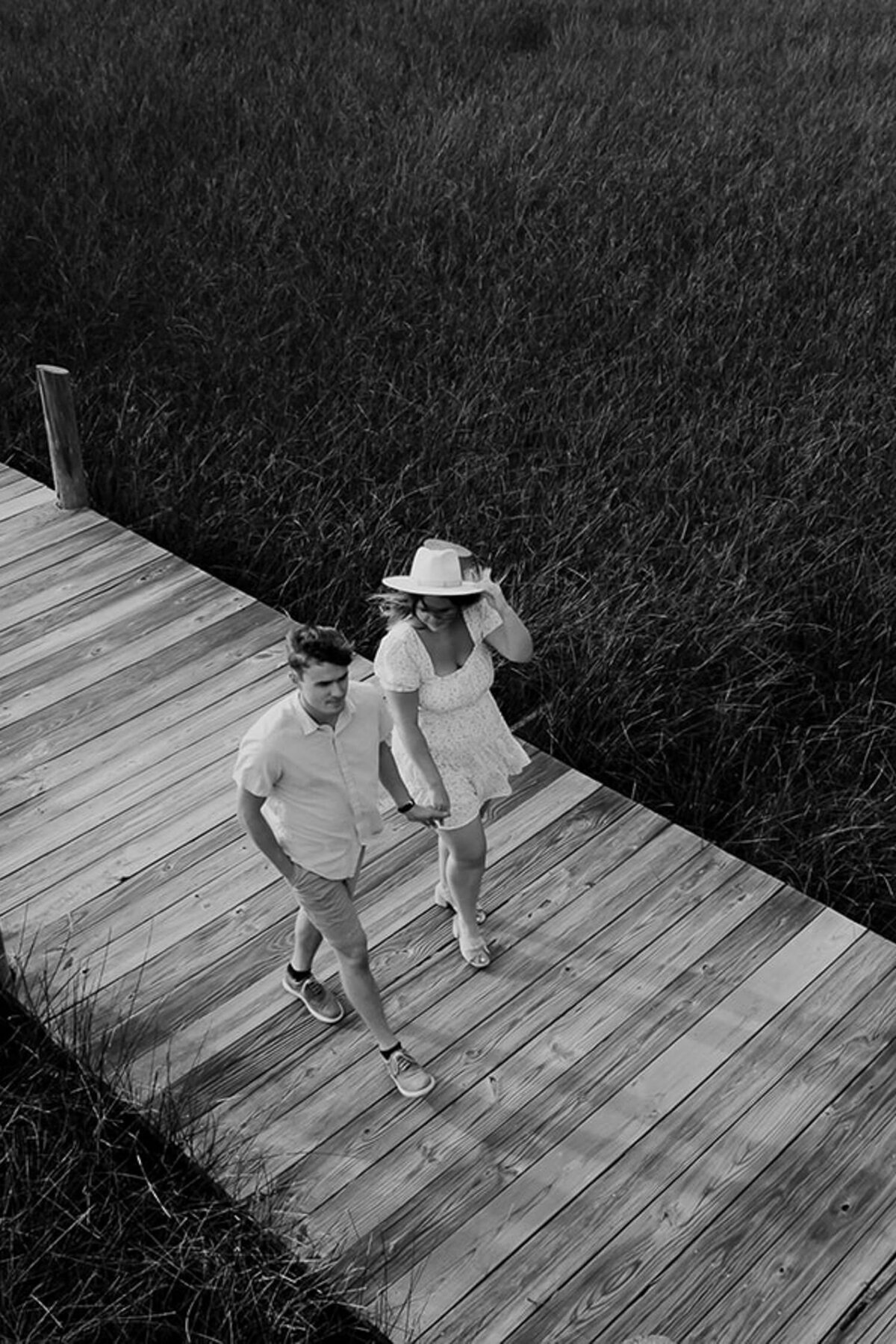 Couple walking in Palmetto Island County Park on wooden boardwalk. Photographed from above with drone. Woman is holding on to her hat