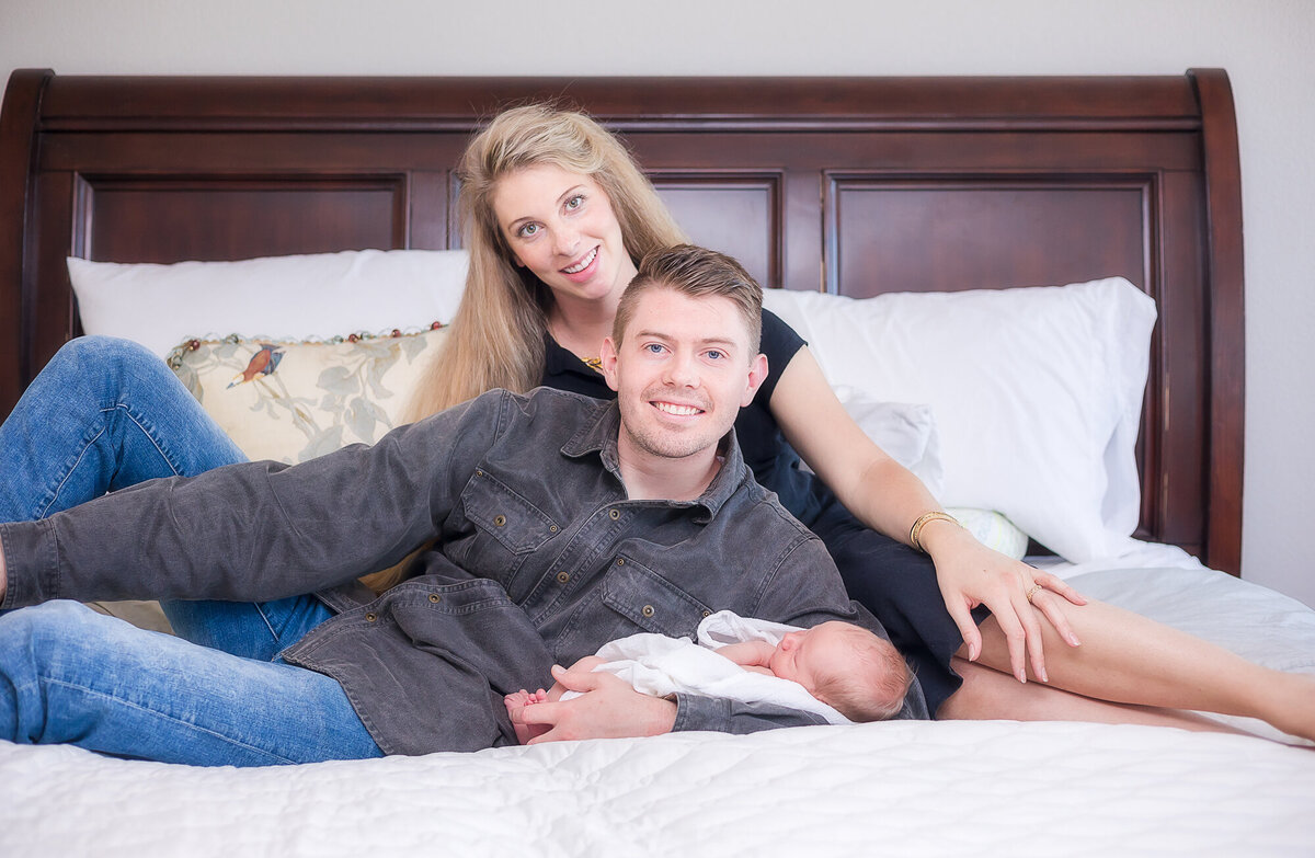 blonde mom, and sandy haired dad holding baby boy on wooden bed