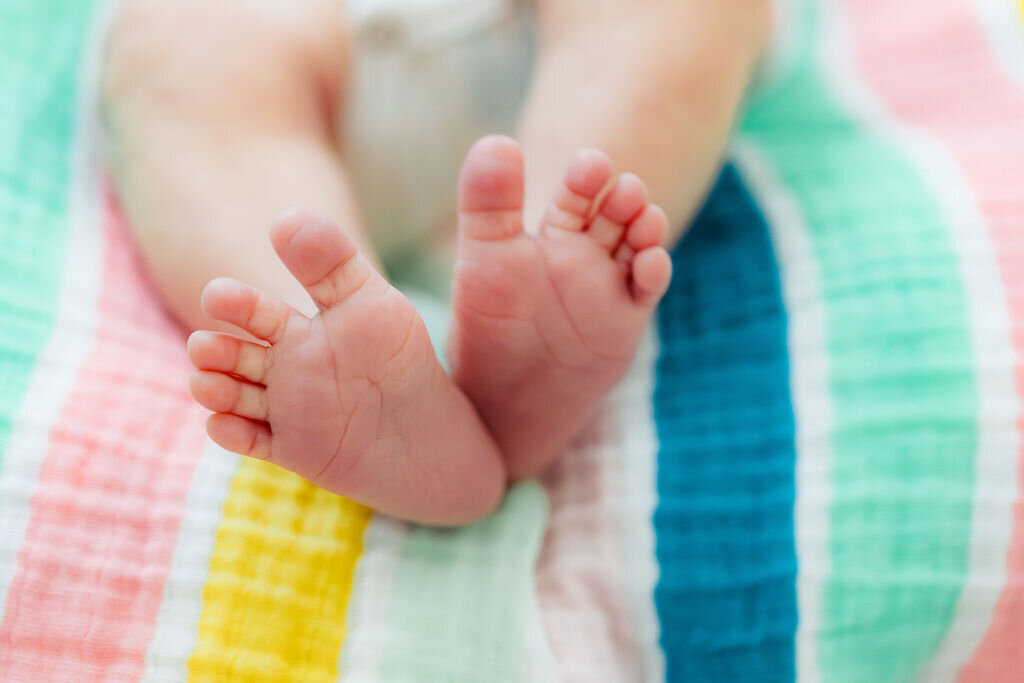 Close up of newborn feet on a rainbow-colored blanket.