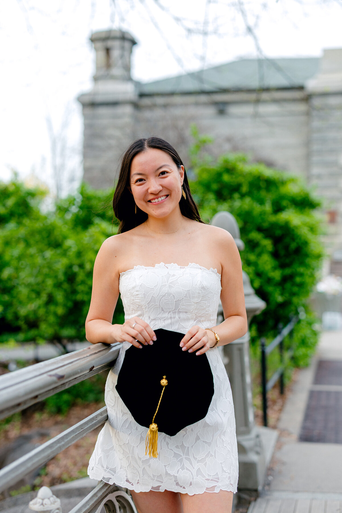 Columbia Law graduate smiling in white dress while holding cap at Central Park.