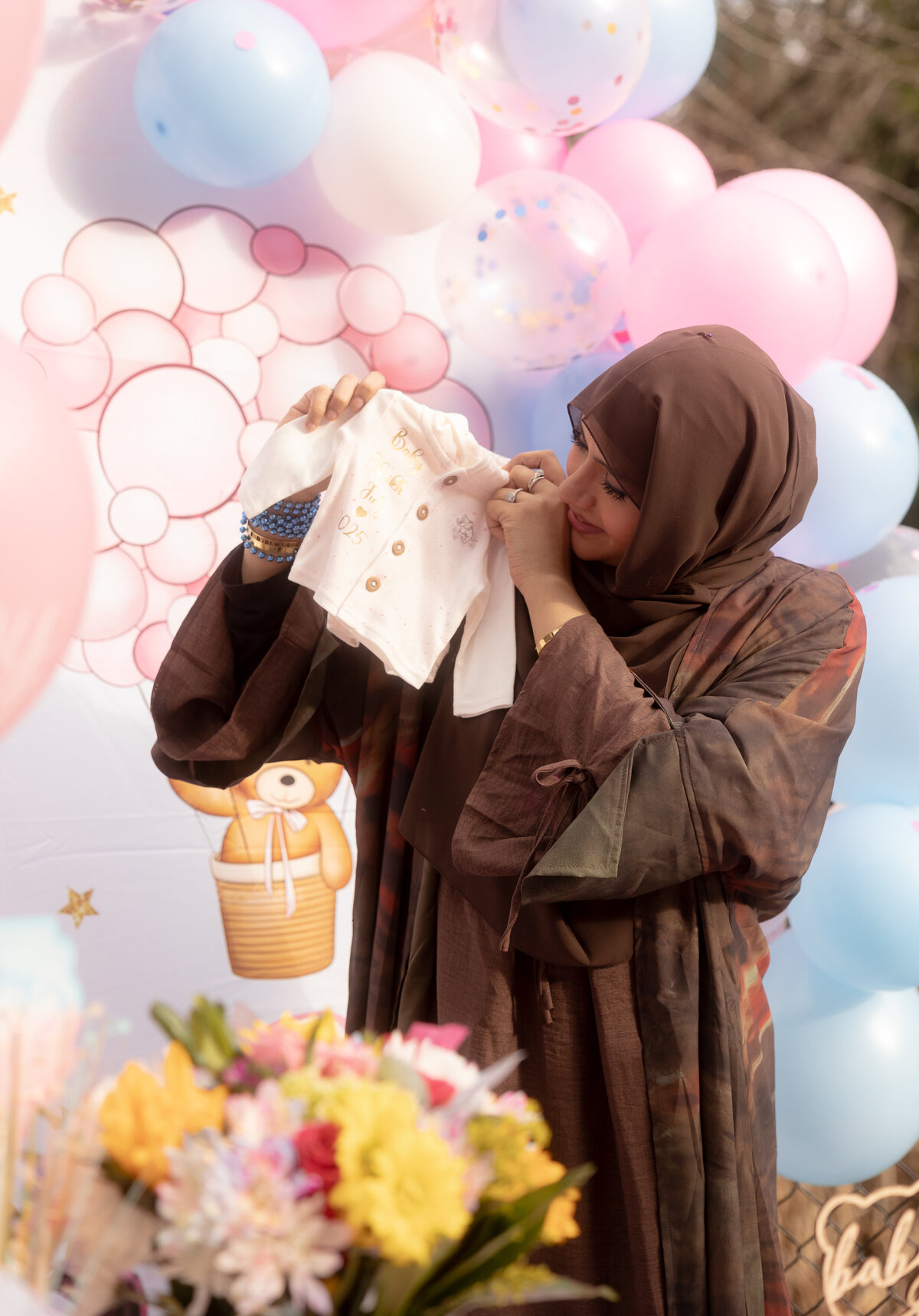 A sweet moment as the mom proudly holds up tiny baby clothes, beaming with happiness and excitement for the new addition to the family.