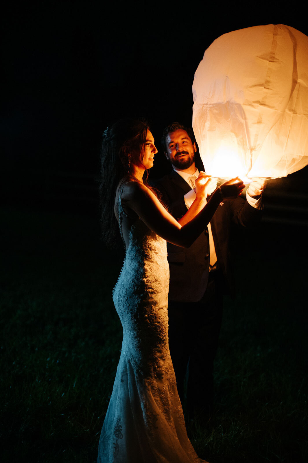 bride and groom lighting paper lanterns at vermont farm wedding at night