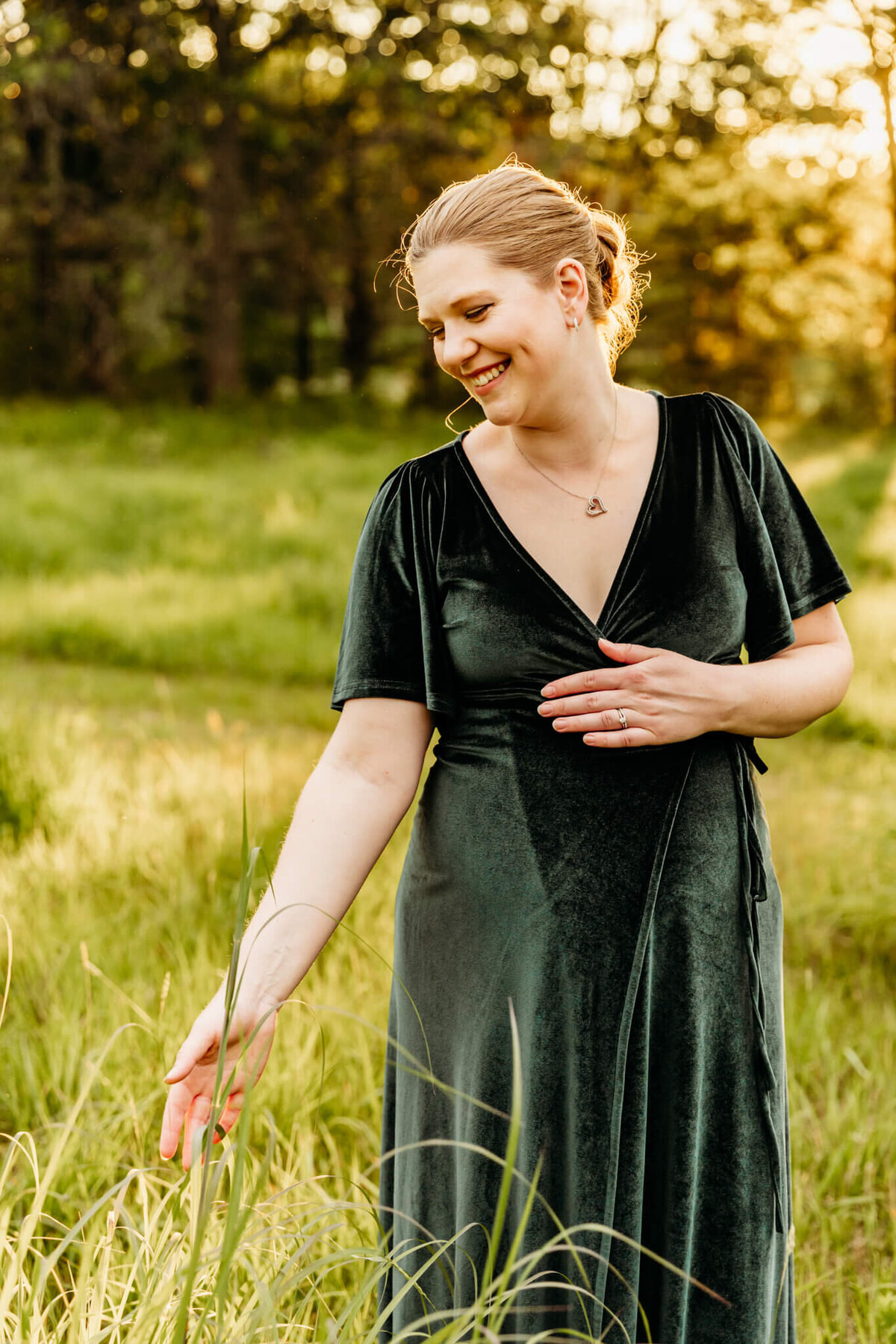 beautiful pregnant mama smiling as she plays with the grass in a field  by Ashley Kalbus