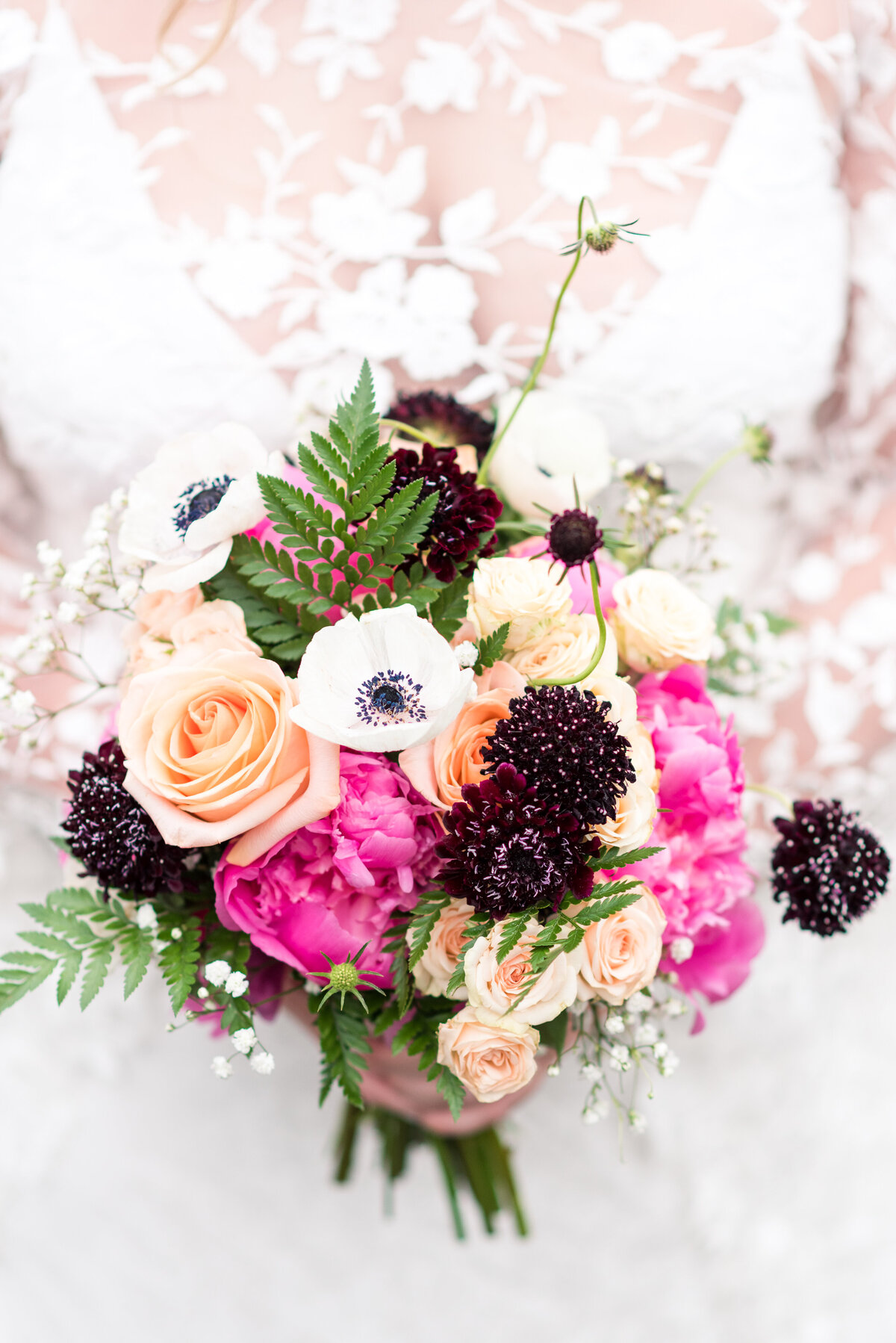 bridal bouquet with bright pink, deep purple and cream florals held by a bride in a lace wedding gown for her rocky mountain national park wedding
