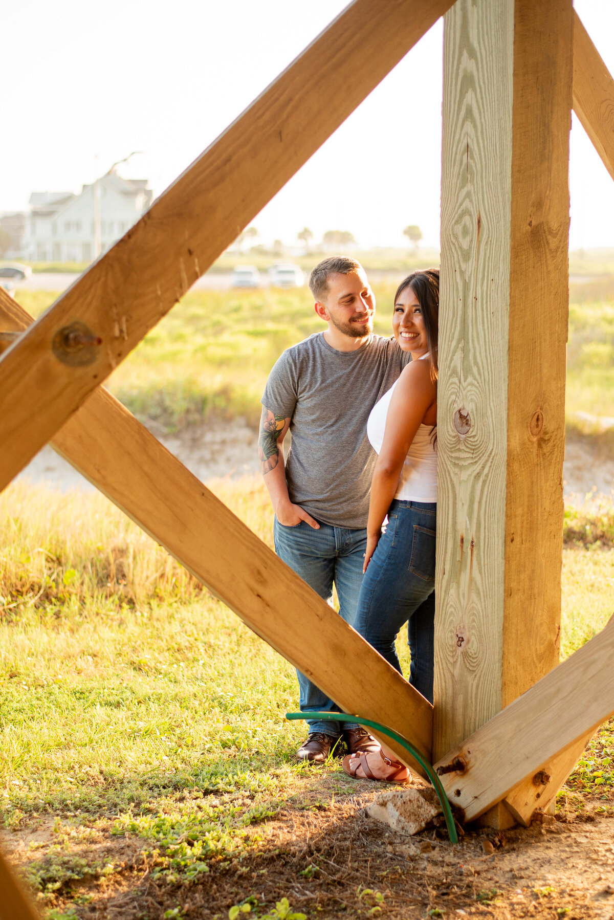 Experience the love and connection of an engagement as this couple leans on a pillar under a pier on the scenic beaches of Galveston, Texas.