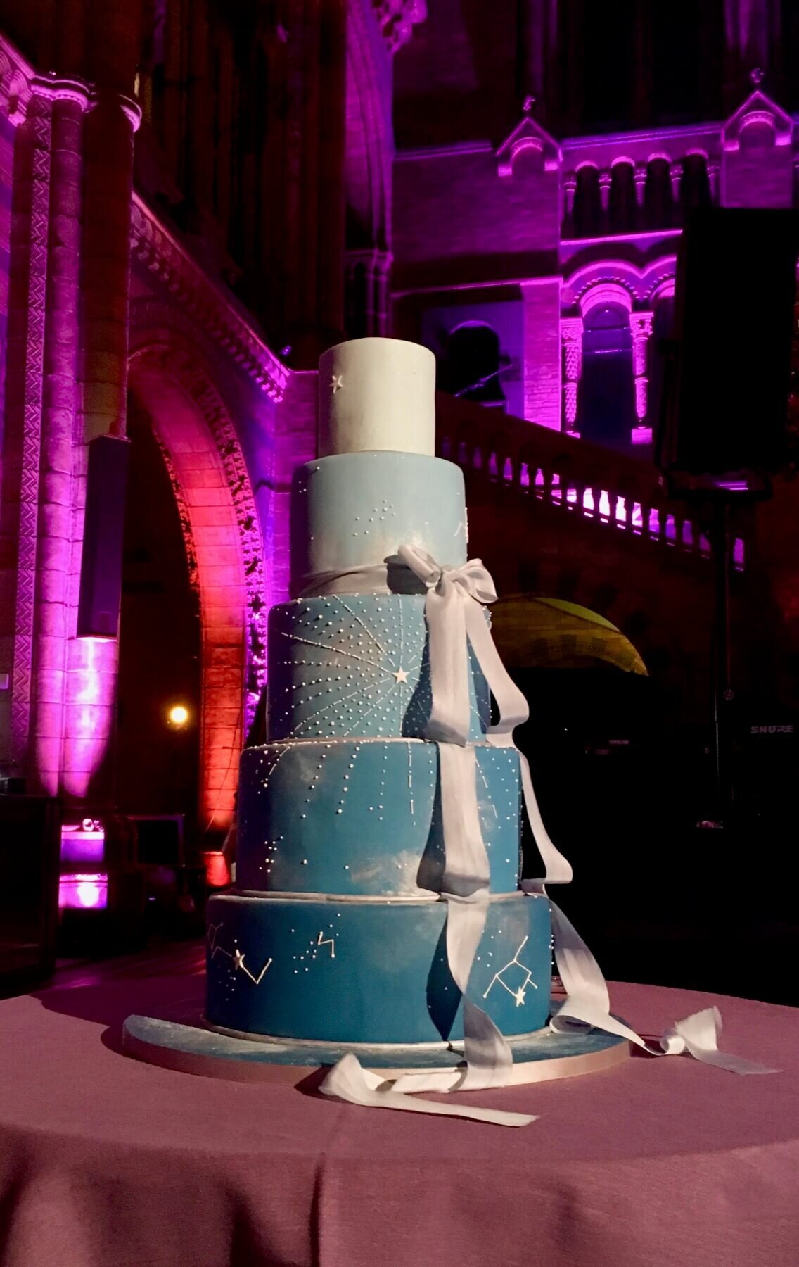 An aqua wedding cake, which is 5 tiers and has star constellations and a huge bow in the middle