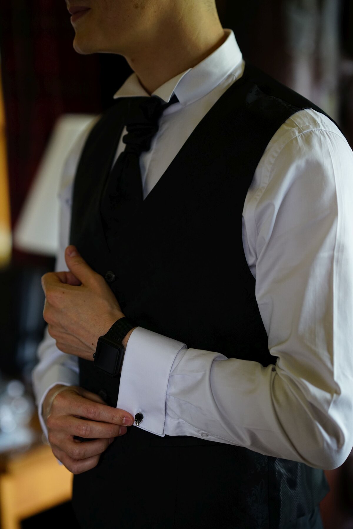 The groom adjusts his cufflinks with a focus on the details of his attire. This close-up image captures a moment of refinement and attention to detail, highlighting the elegance and sophistication of his wedding outfit.