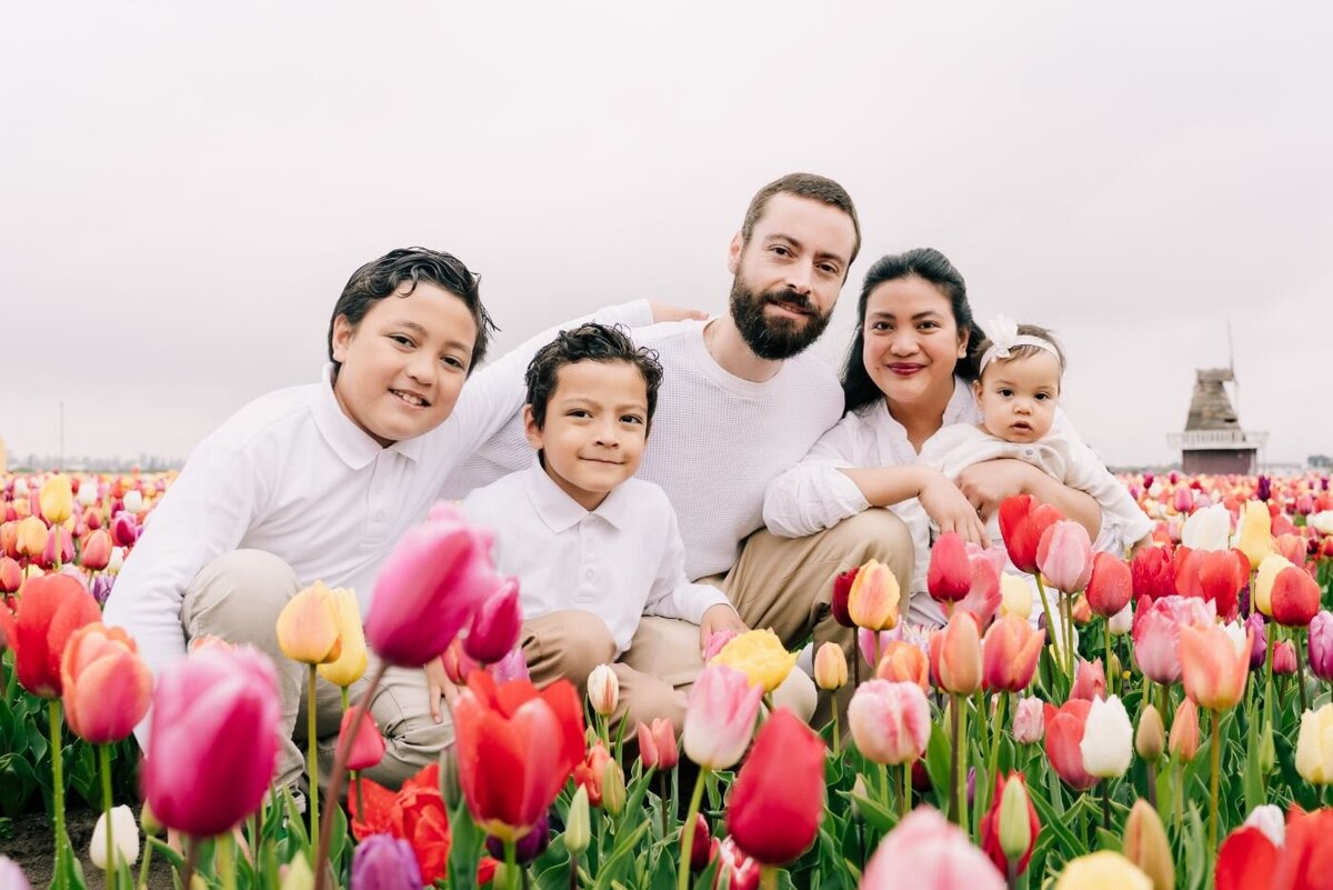 Family in tulip field – Parents with three children dressed in white posing happily among bright spring tulips with a classic Dutch windmill in the distance.