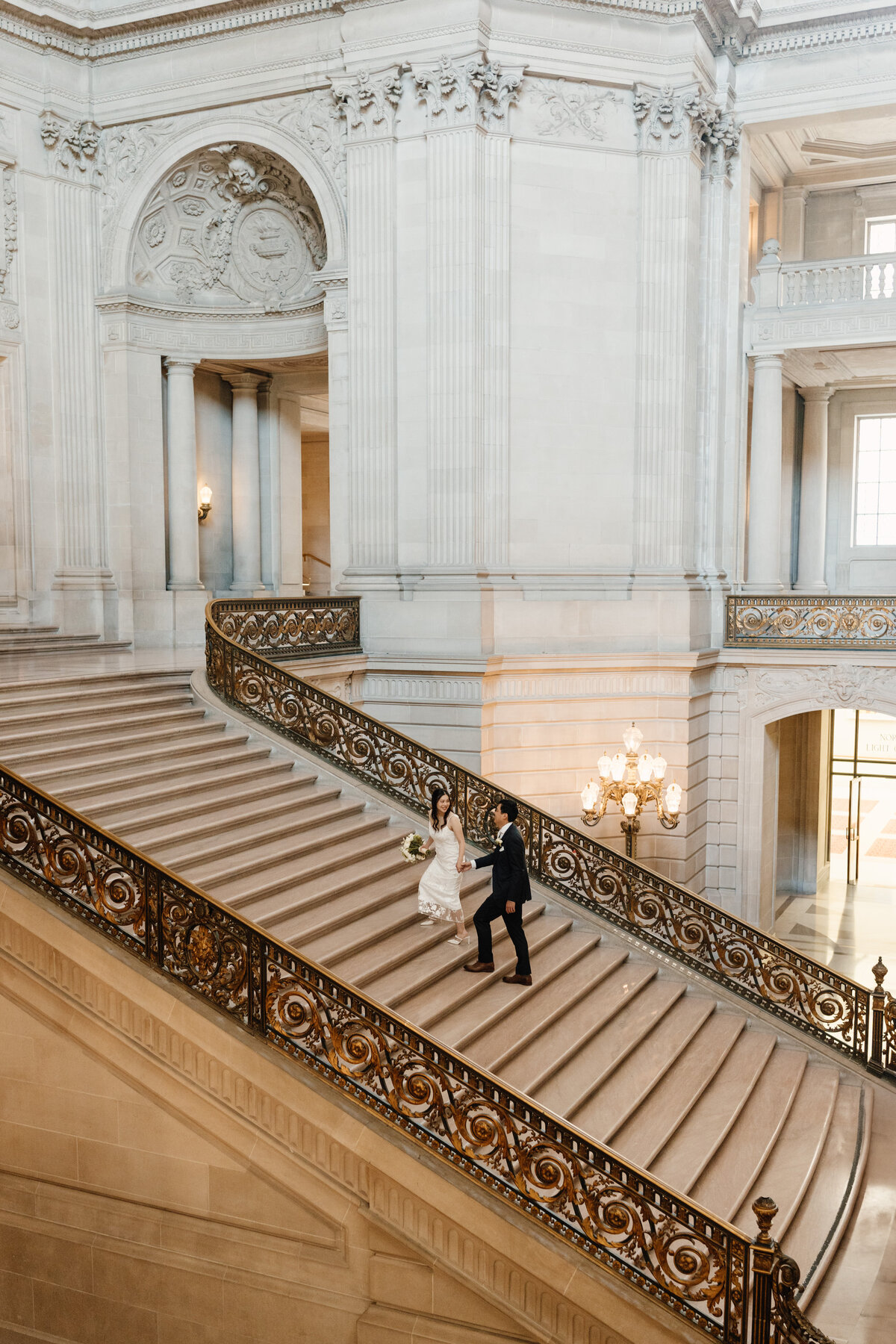 bride and groom walk up steps of san francisco city hall