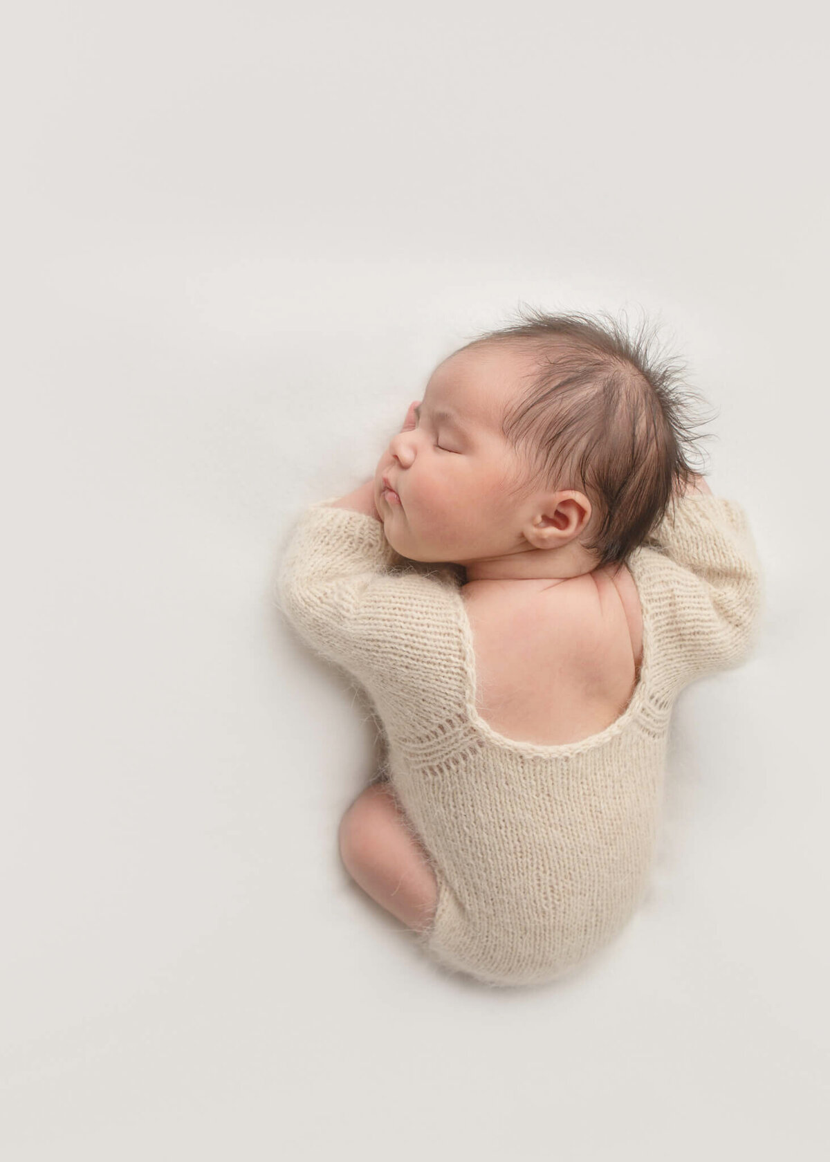 Newborn baby in cream romper laying on a white blanket asleep on her hands by Los Angeles Newborn Photographer