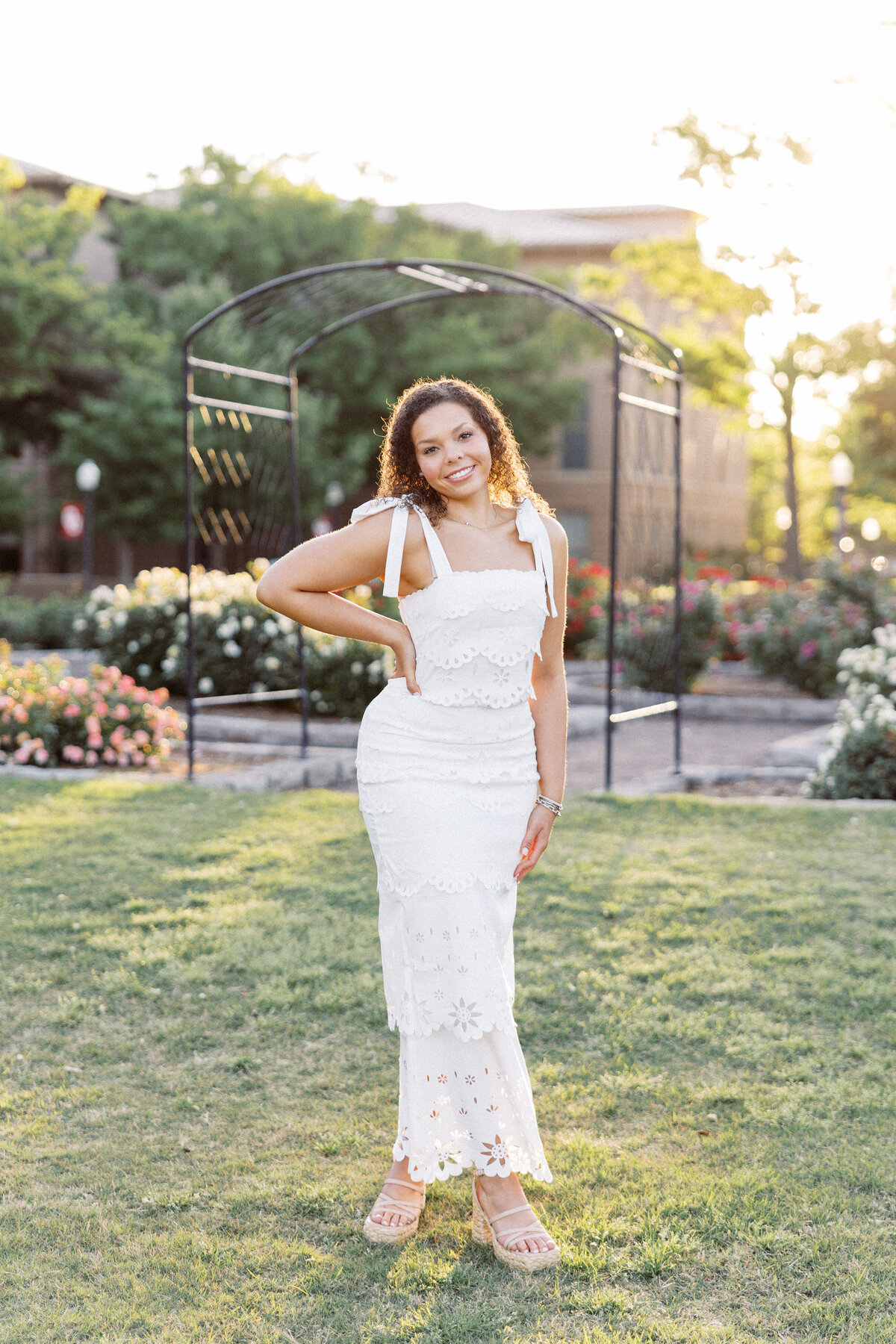 college senior girl holds hand on hip in front of ou rose garden at sunrise