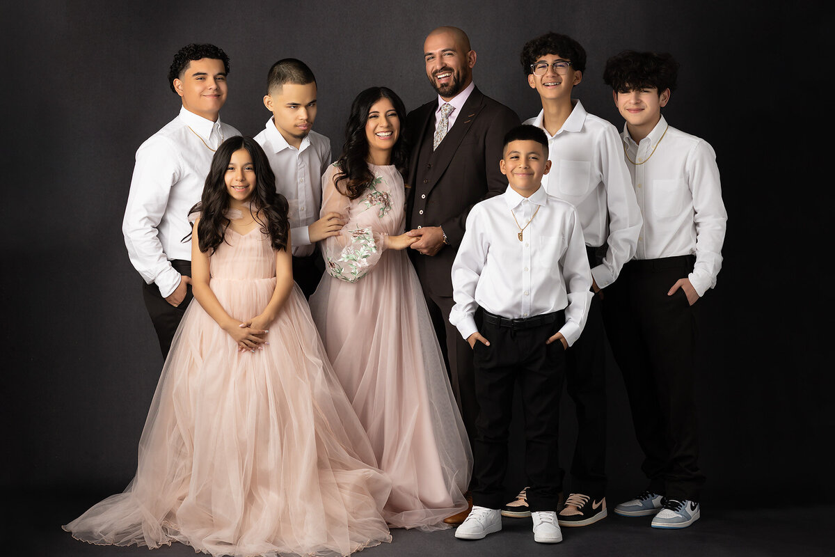 A loving family captured by a Dallas family photographer, smiling together in coordinated outfits against a dark backdrop, highlighting the warmth and unity of their bond.