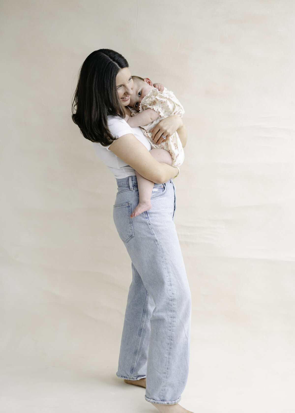Mom in a classic outfit of a t-shirt and jeans snuggling her little baby