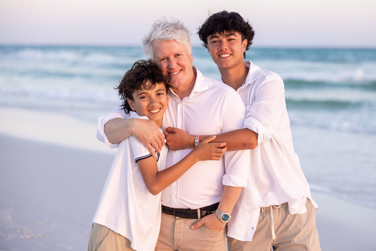 father and sons hugging on the beach at Watercolor, Florida.