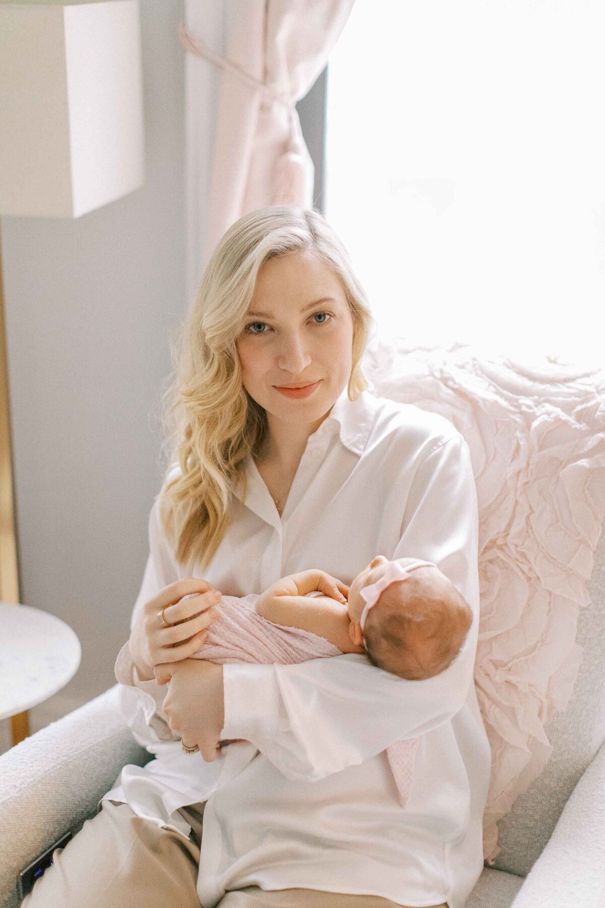 blonde mom holding her beautiful baby girl and sitting on a pink rocking chair