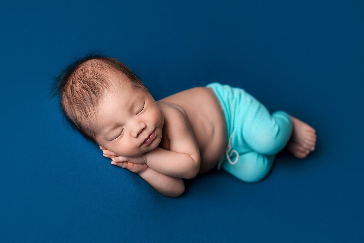 Vancouver newborn photoshoot of baby boy in teal in sidelaying beanbag pose