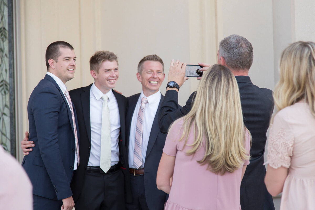 a man taking a picture with a phone of 3 men in suits