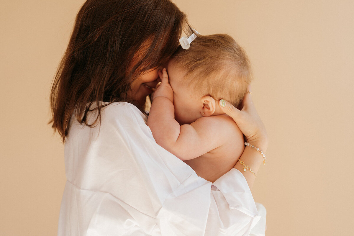 woman holds baby close to her face couple smiling holding two kids during newborn photoshoot captured by NYC newborn photographer Elsie Goodman 
