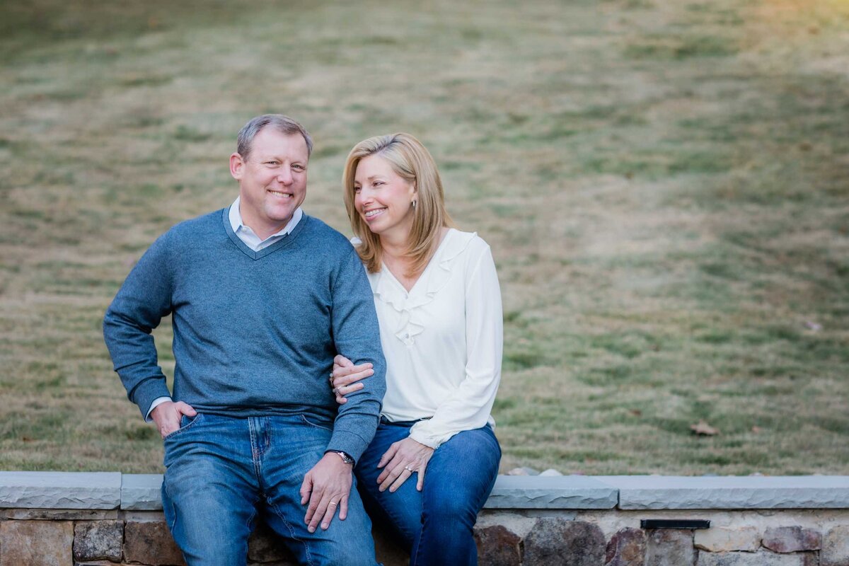 A woman smiling at her husband lovingly and holding his arm while they sit on a stone wall.