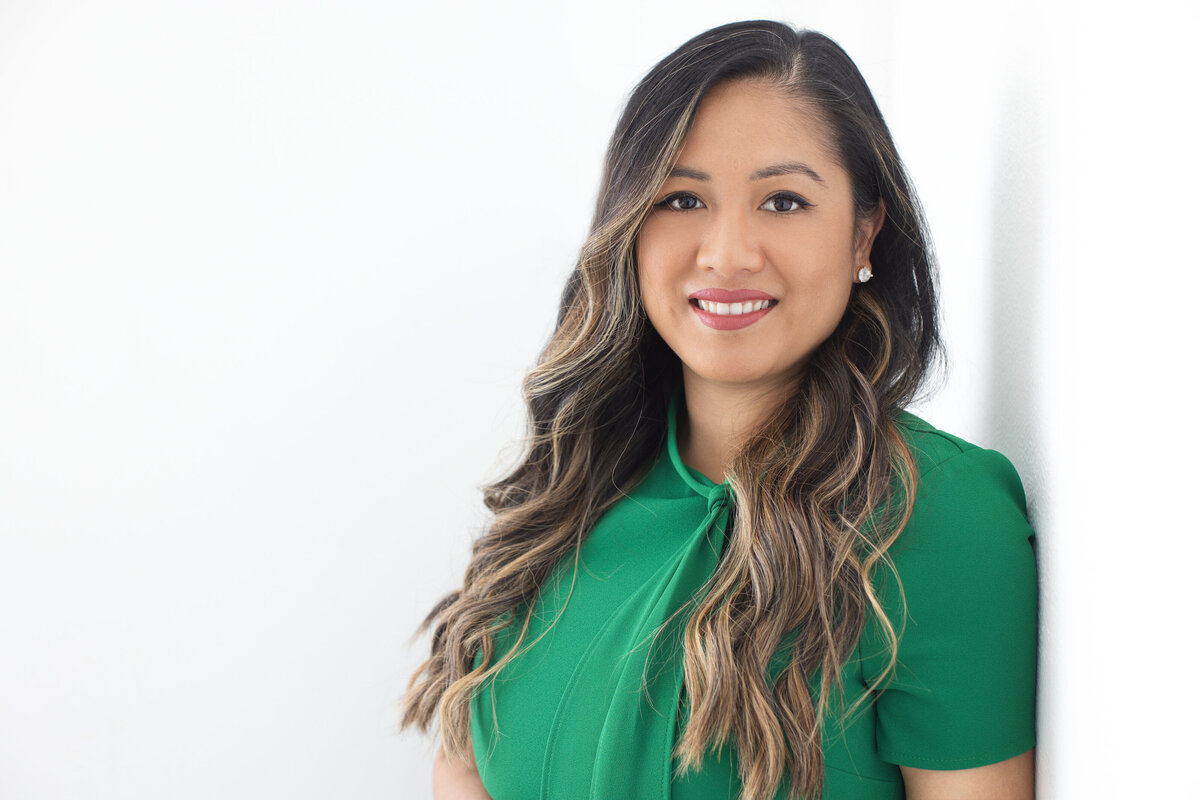 An Asian woman in a green dress smiles as she poses for a professional headshot picture on a white background for Janel Lee Photography studios in Cincinnati Ohio
