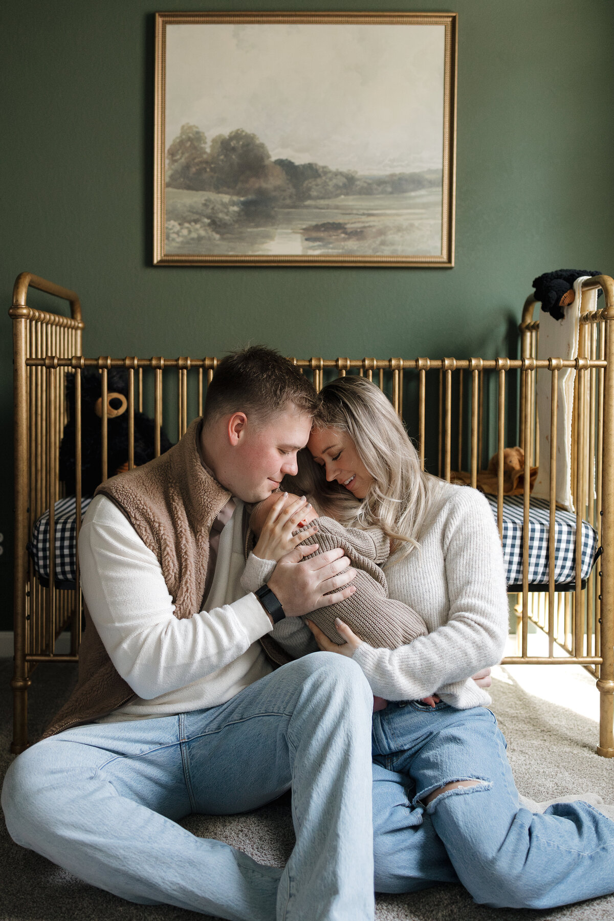 Longmont colorado family sitting with newborn in front of brass crib looking down at baby during in home newborn session