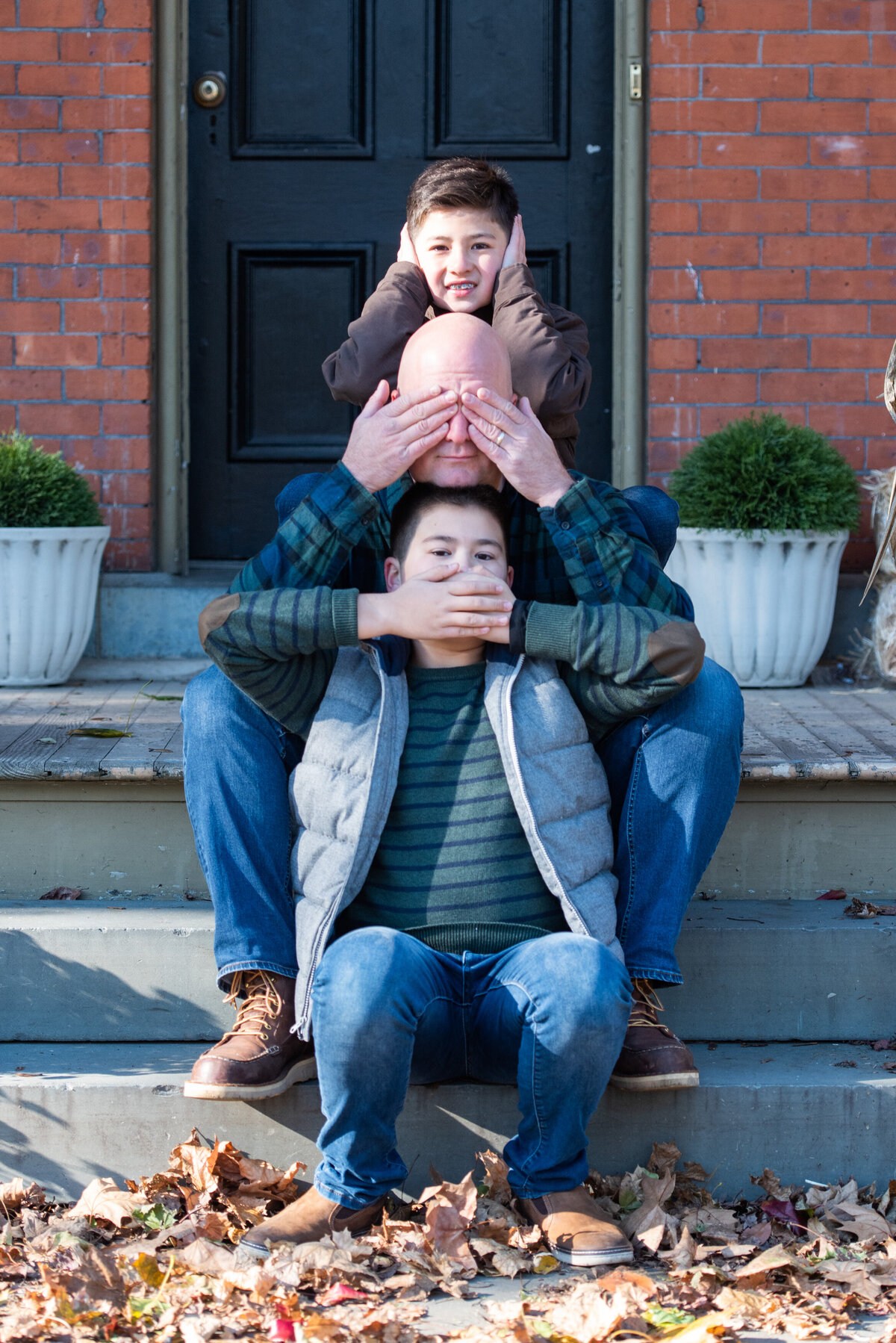 A dad and two sons sitting on steps while one covers their mouth, another their eyes, and the third their ears