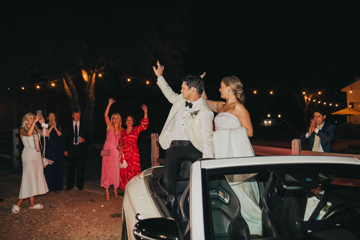 bride and groom wave to their friends and family as they leave the reception