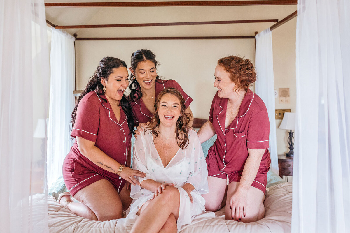Bridal party with bride on four post bed having a joyful moment in the getting ready room at Cobb Hill Estate by Lisa Smith Photography