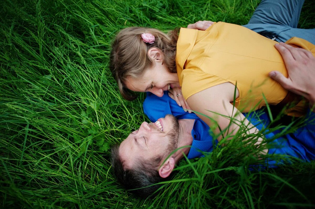 a couple wearing yellow and blue lay in the tall green grass