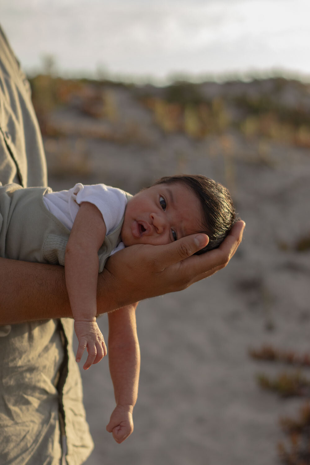 Close-up of a father holding his newborn baby in one hand while standing on the beach