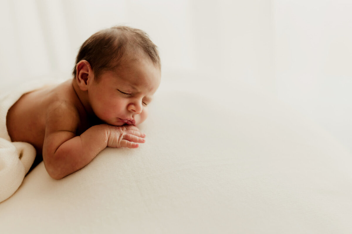 Newborn baby boy sleeps with his hands under his chin.