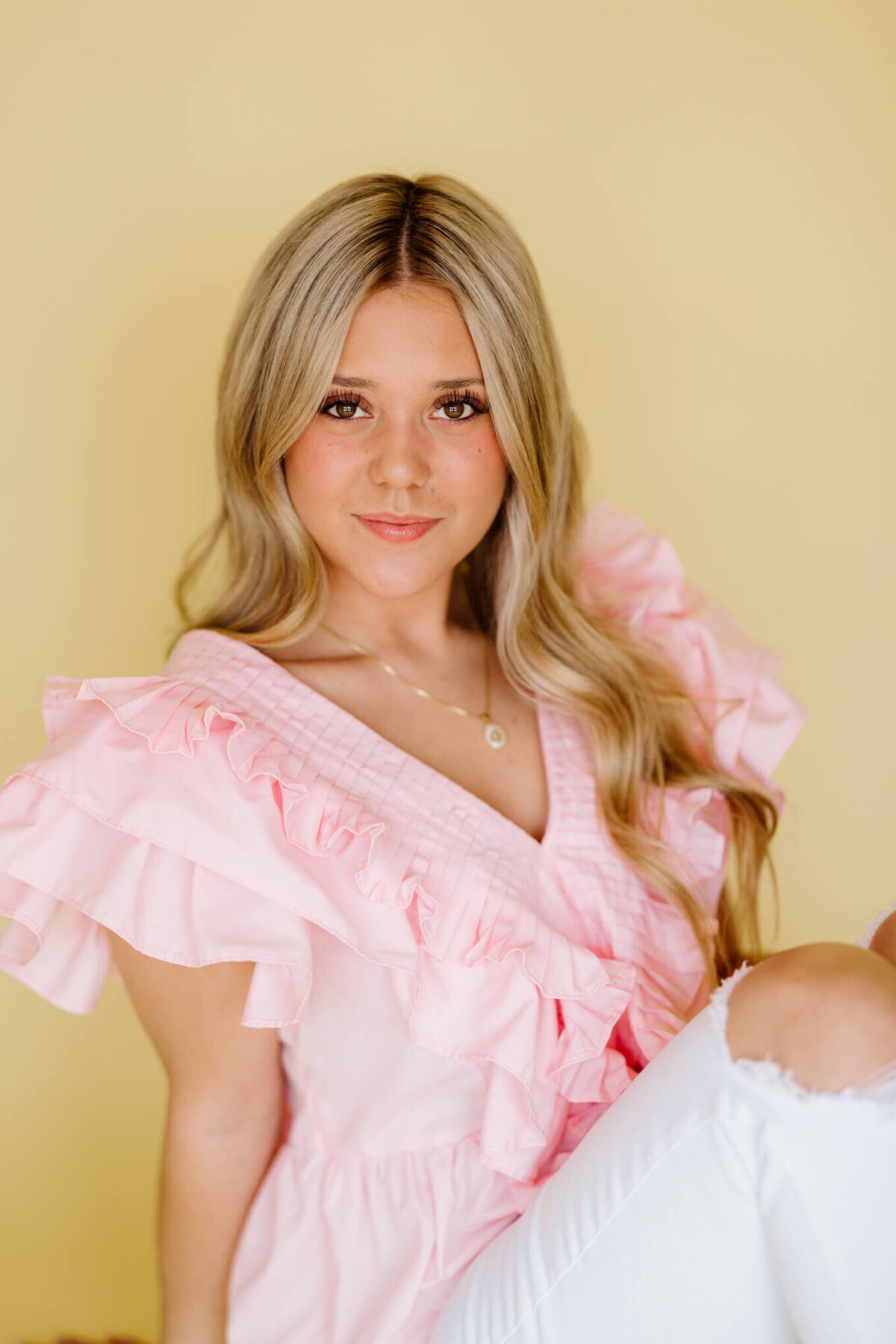 fun and vibrant sorority headshot of TCU student in pink and white sitting in front of yellow wall